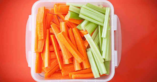 Carrots and Celery in a plastic container on an orange table
